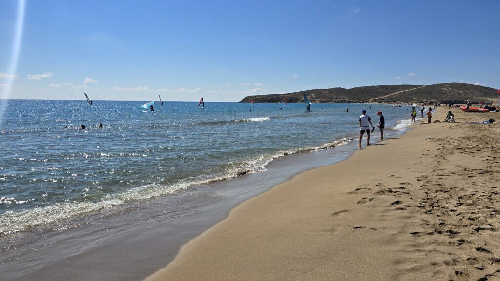 Prasonisi Rodi: Dove i Due Mari Si Incontrano (Prezzi e Consigli) 4 Spiaggia Prasonisi lato Mar Mediterraneo con onde tranquille, sabbia soffice e surfisti in lontananza.